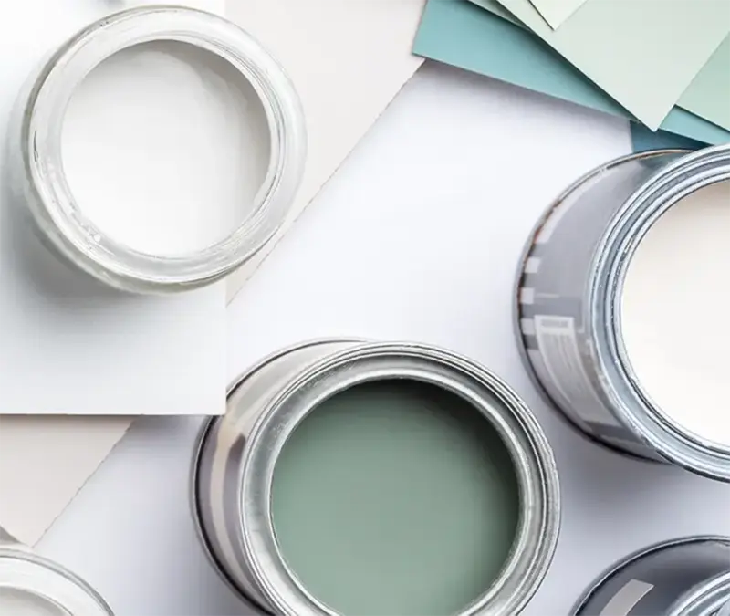 Open paint cans with neutral and green paint colors beside paper color swatches for a painting services website.