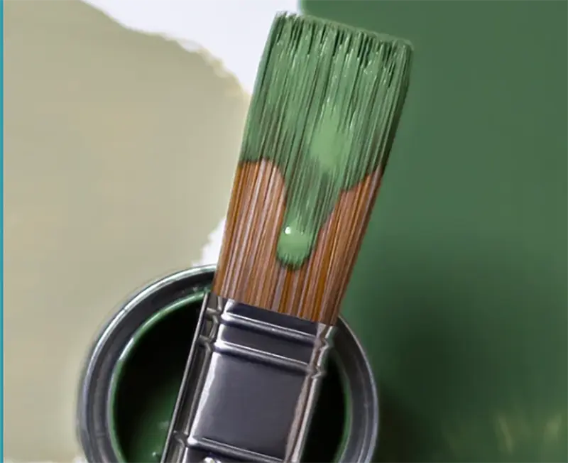 Close-up of a paint brush dipped in green paint beside an open paint can.