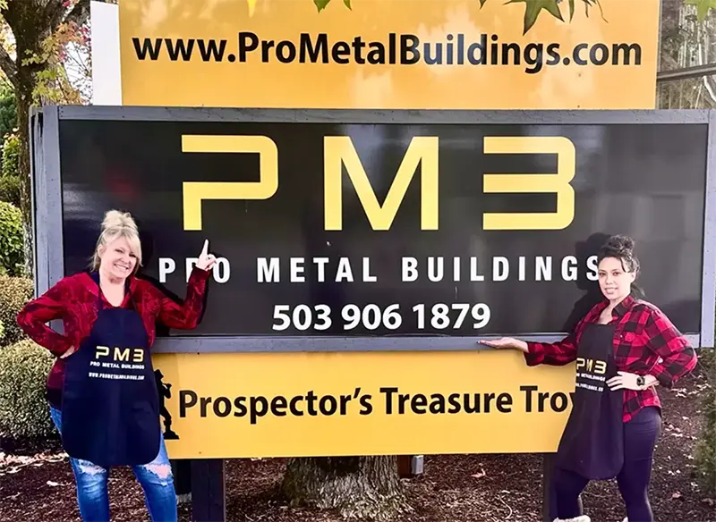 Pro Metal Buildings team members standing beside a PMB branded sign with the company website and phone number.