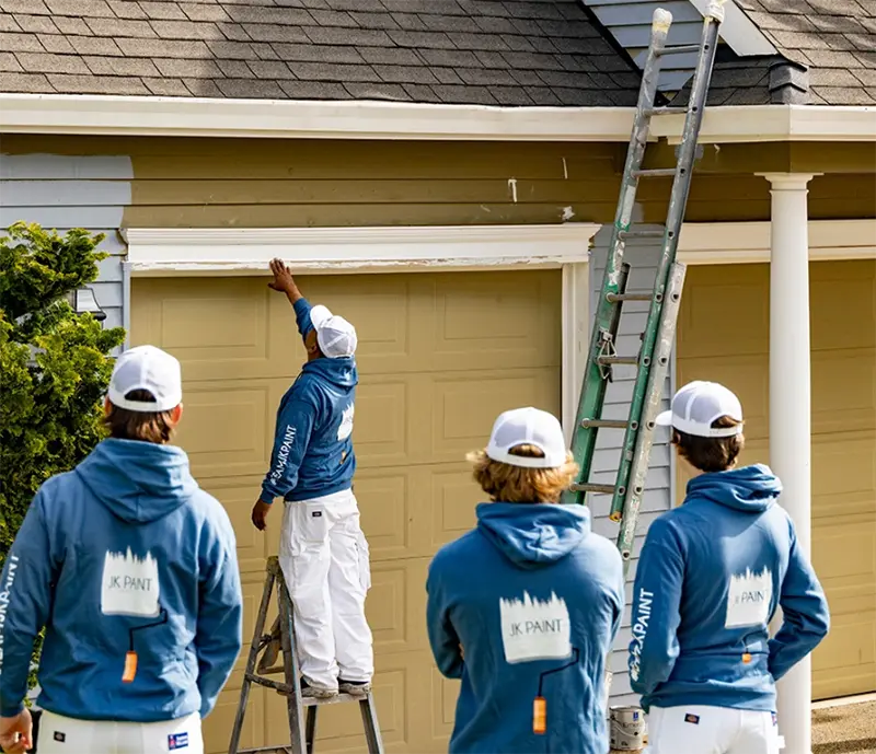 Painting crew inspecting and preparing a home exterior near the garage before repainting.
