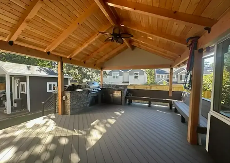 Covered backyard deck with wood ceiling, outdoor kitchen, and built-in bench seating.